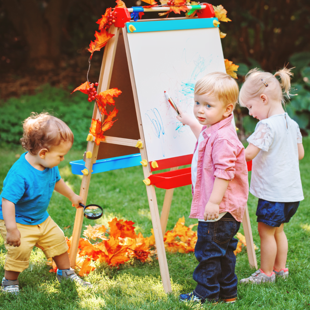 Three children playing outdoors, painting, playing with autumn leaves